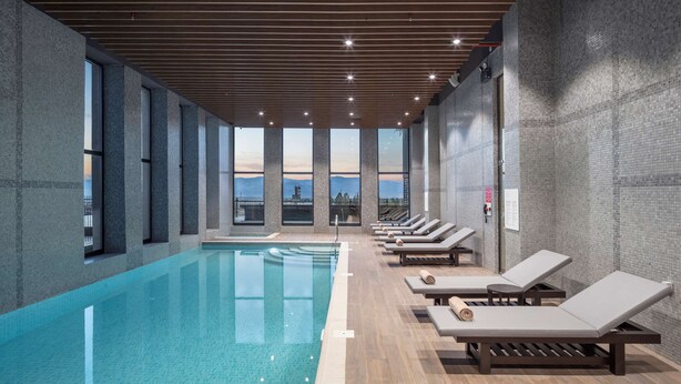 Una piscina interior con sillones de descanso y grandes ventanales con vistas a la ciudad.