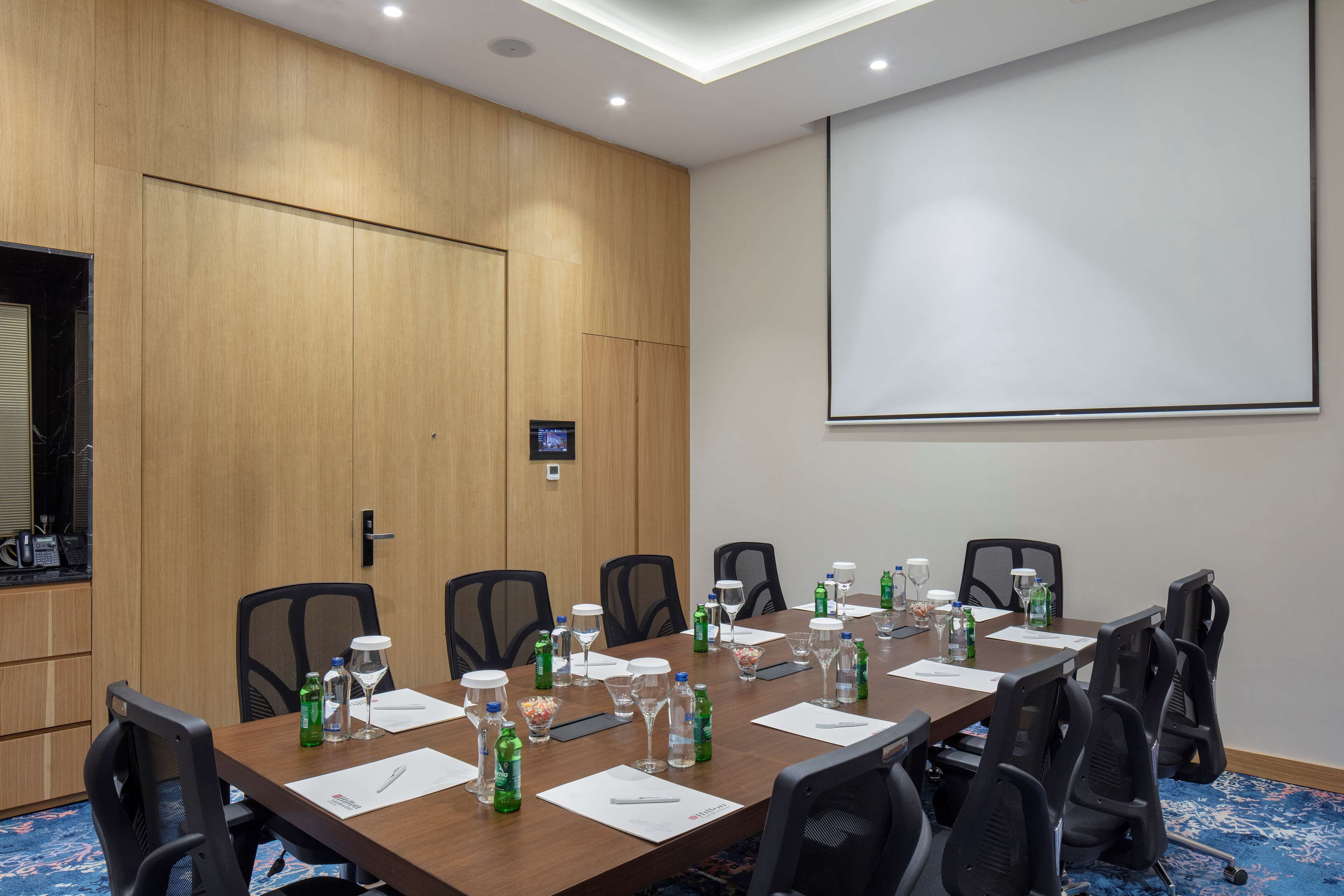 A conference room with a long table, chairs, water bottles, glasses, and a projector screen.