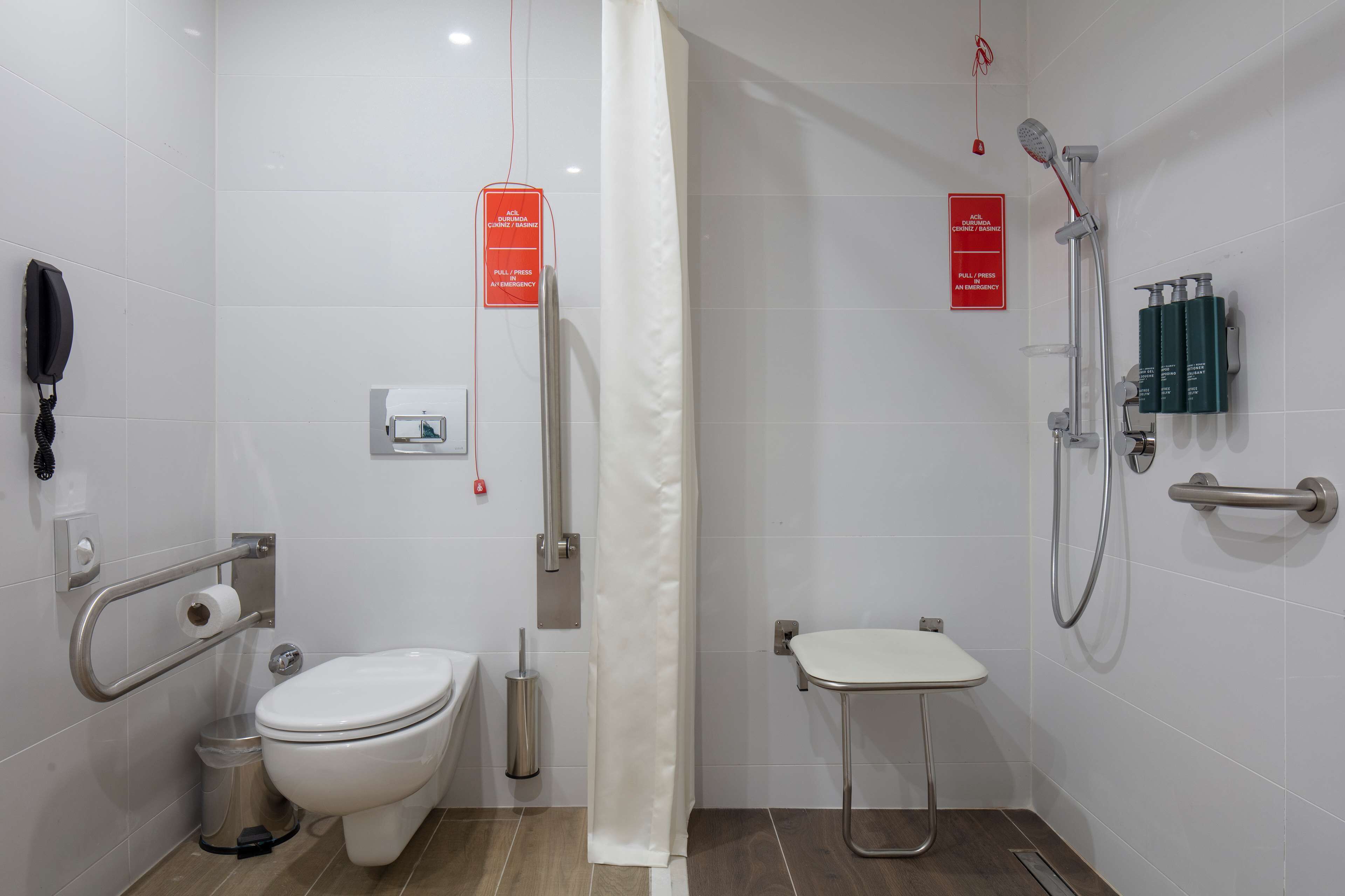 A modern bathroom with a toilet, bidet, shower, and handrails.