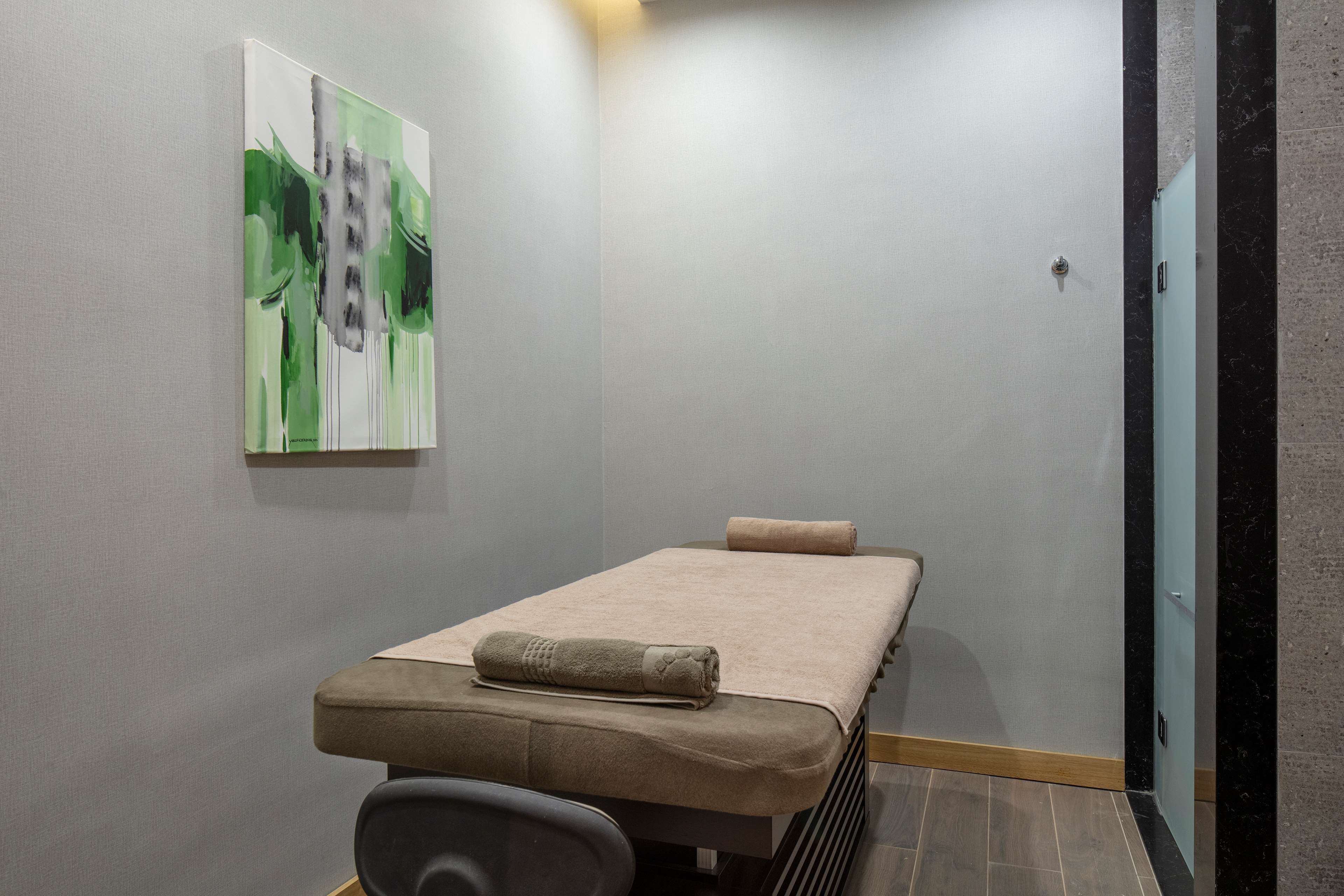 A massage room with a massage table, towels, and a painting on the wall.