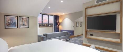 A hotel room with a large bed, a sofa, a TV, and a city view.