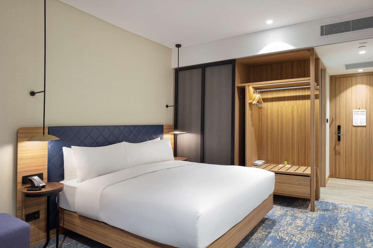 Ein Hotelzimmer mit Bett, Nachttisch, Lampe und Kleiderschrank.