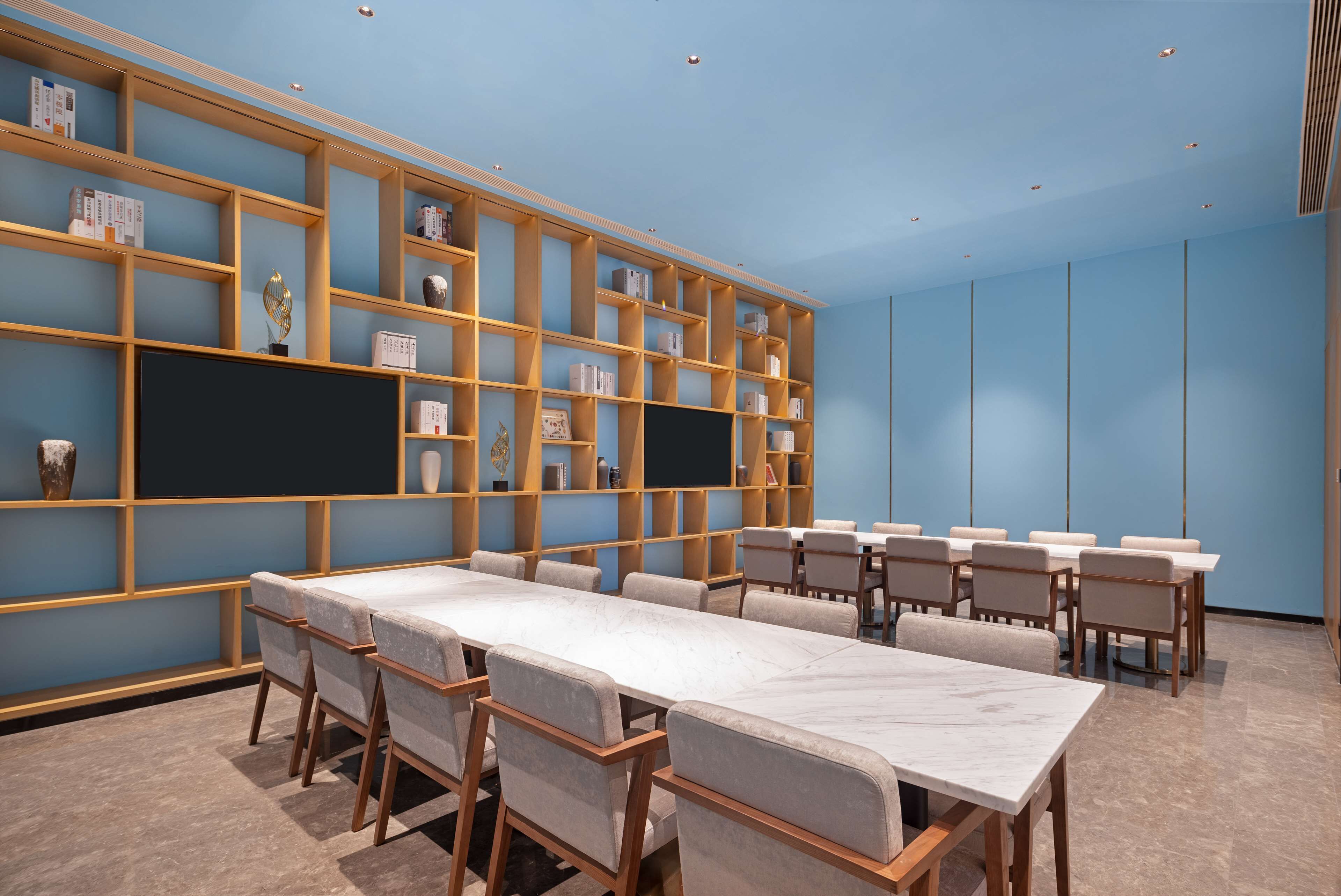 Un salón de conferencias con una larga mesa, sillas y una estantería llena de libros y objetos decorativos.