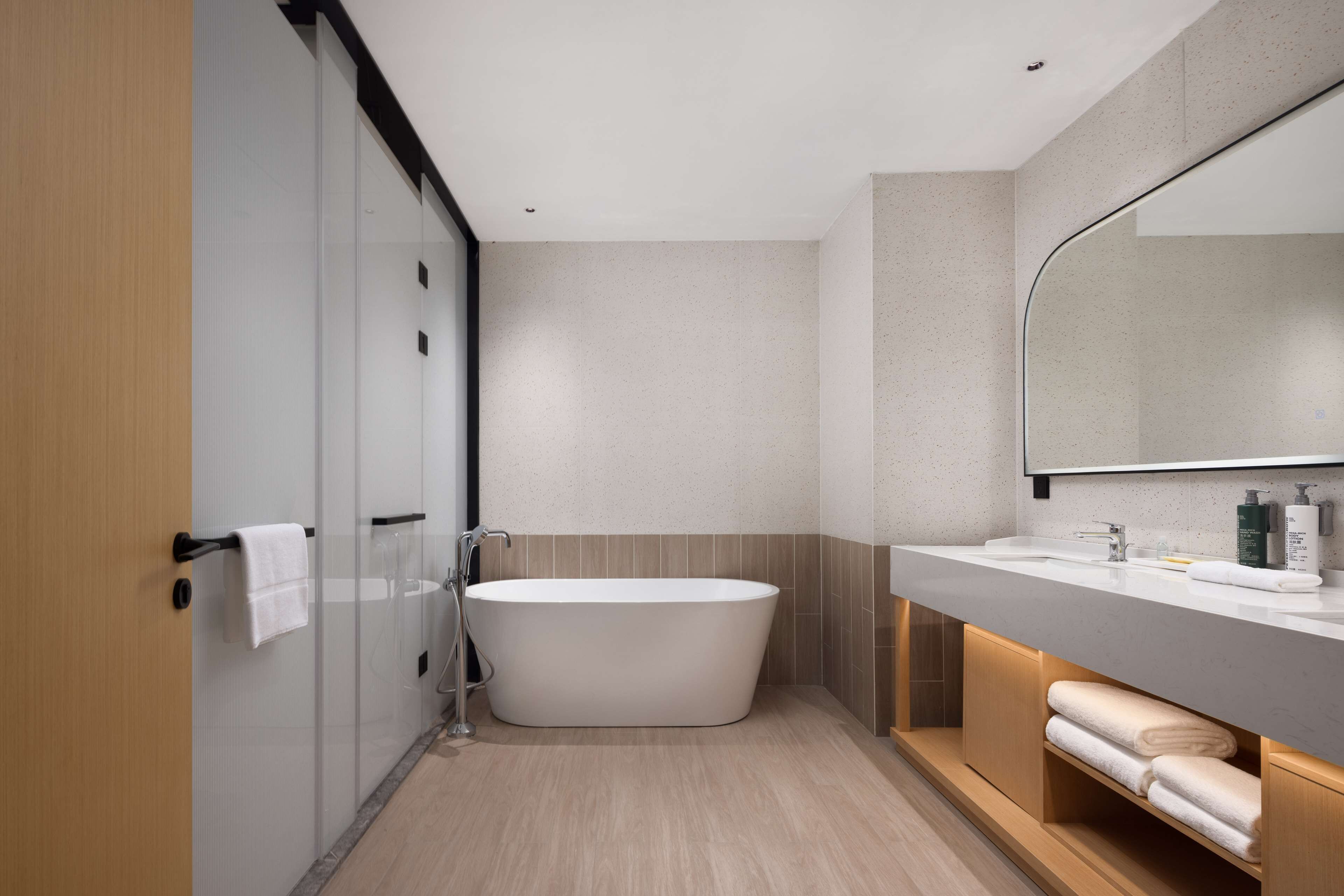 A modern bathroom with a freestanding bathtub, a large mirror, and a vanity with a sink and towel storage.