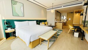 A modern hotel room with a large bed, bedside tables, a desk, a chair, a mirror, and a bathroom area.