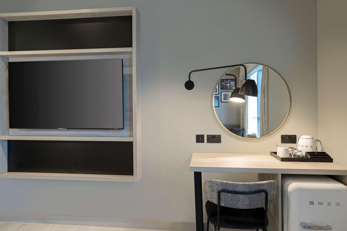 A modern room with a desk, chair, and a small kitchenette area.