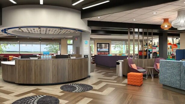 A modern lobby with a reception desk, seating area, and large windows offering a view of the outdoors. - Tru by Hilton Chesterfield Township Detroit (New Baltimore)