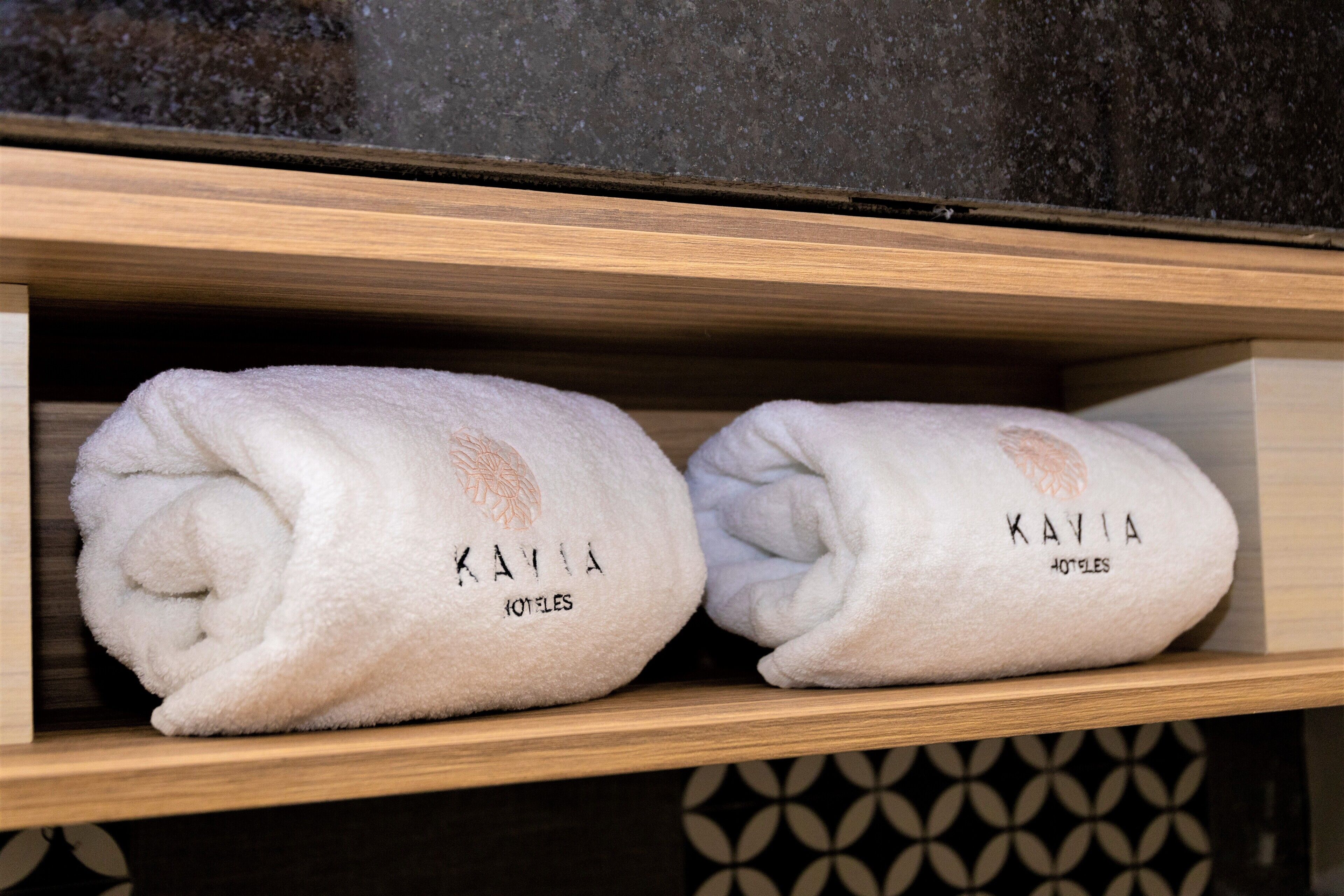 Dos toallas dobladas ordenadamente sobre un estante de madera, con el texto "KAVIA HOTELS".