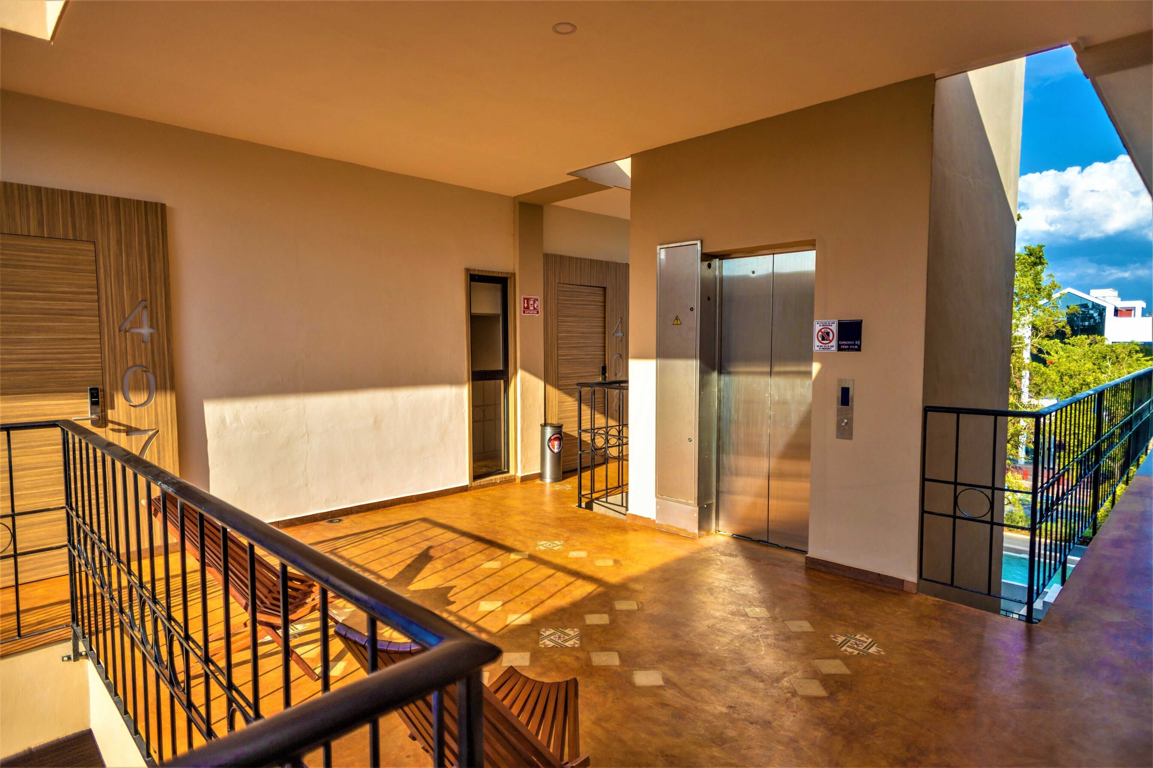 A spacious indoor area with a wooden floor, metal railing, and a view of a building outside.