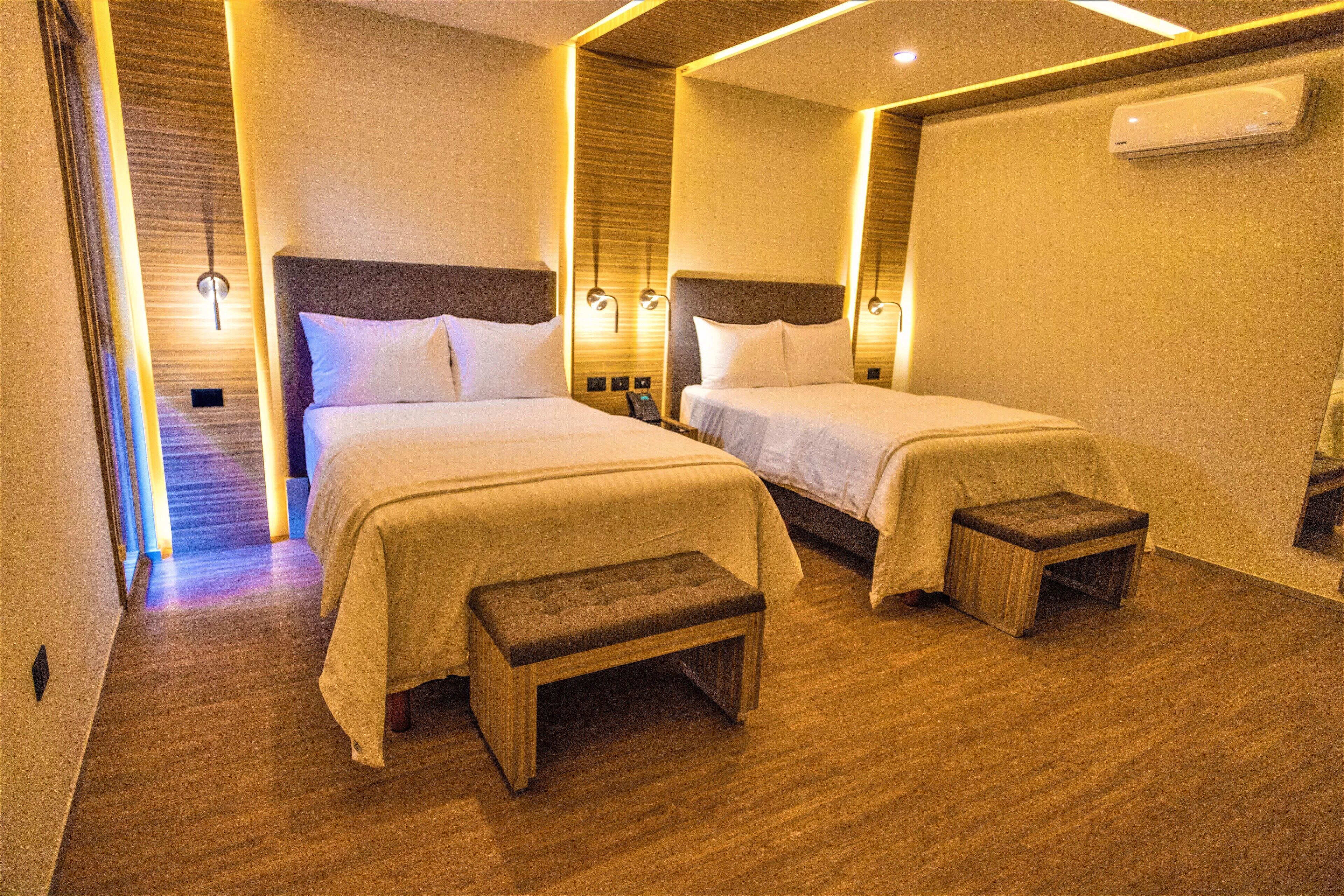 Une chambre d’hôtel avec deux lits, un plancher en bois et un banc.