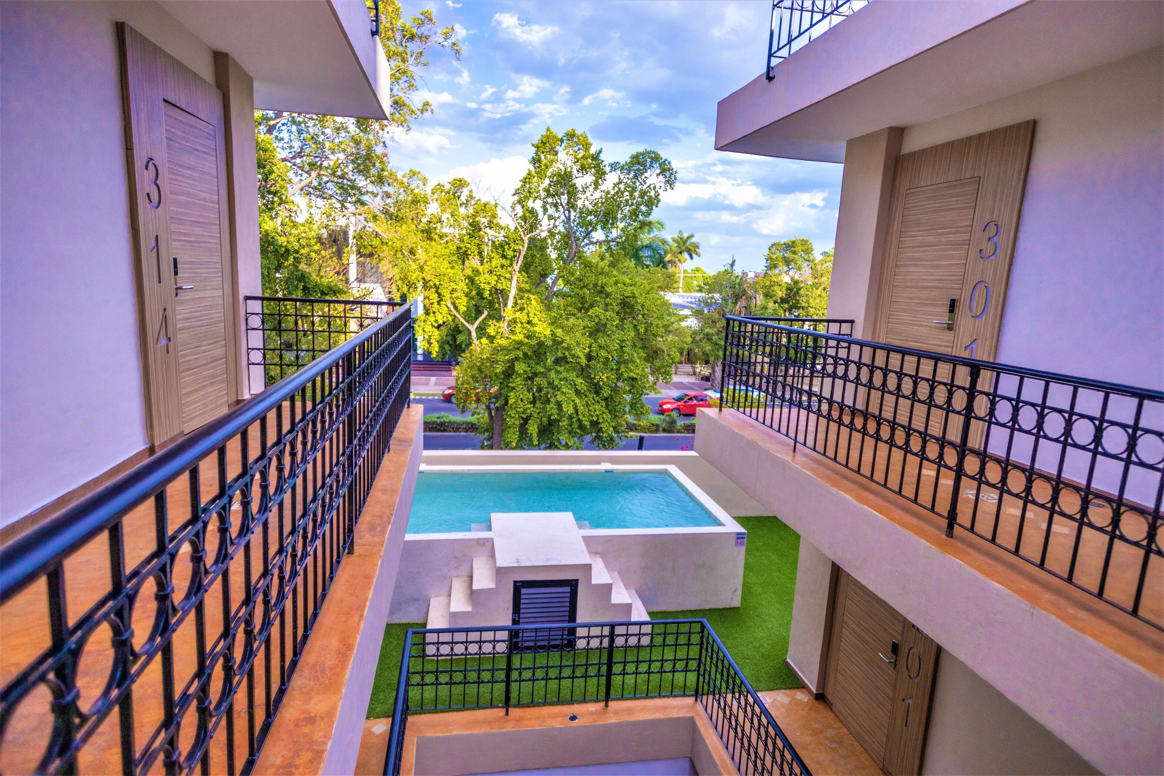 A multi-level building with a swimming pool, balconies, and a gated entrance.