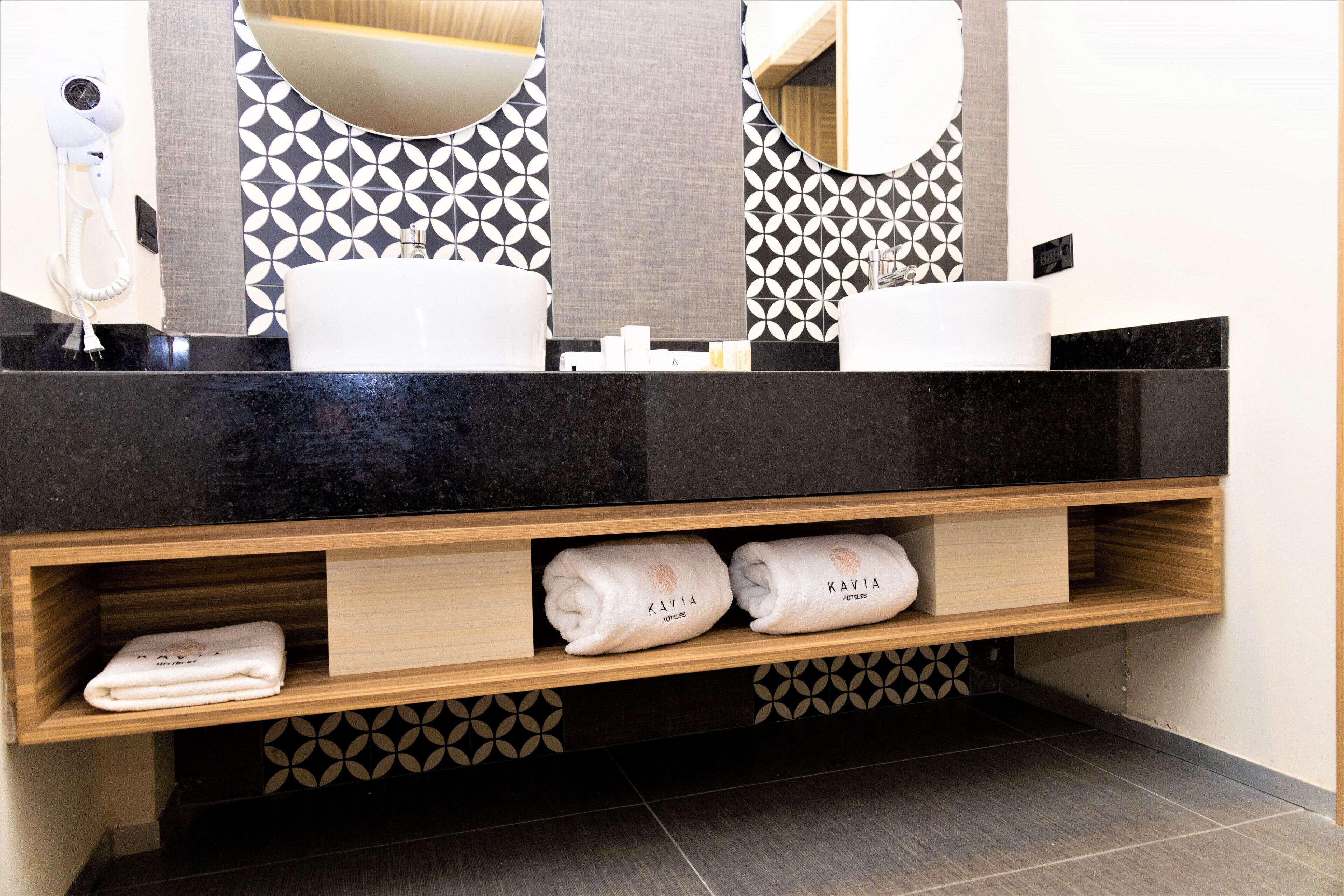 Une salle de bain moderne avec un plan de toilette noir, deux vasques et un meuble-lavabo en bois agrémenté de serviettes.
