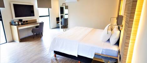 A modern hotel room with a large bed, a desk with a chair, a flat-screen TV, and a large window.