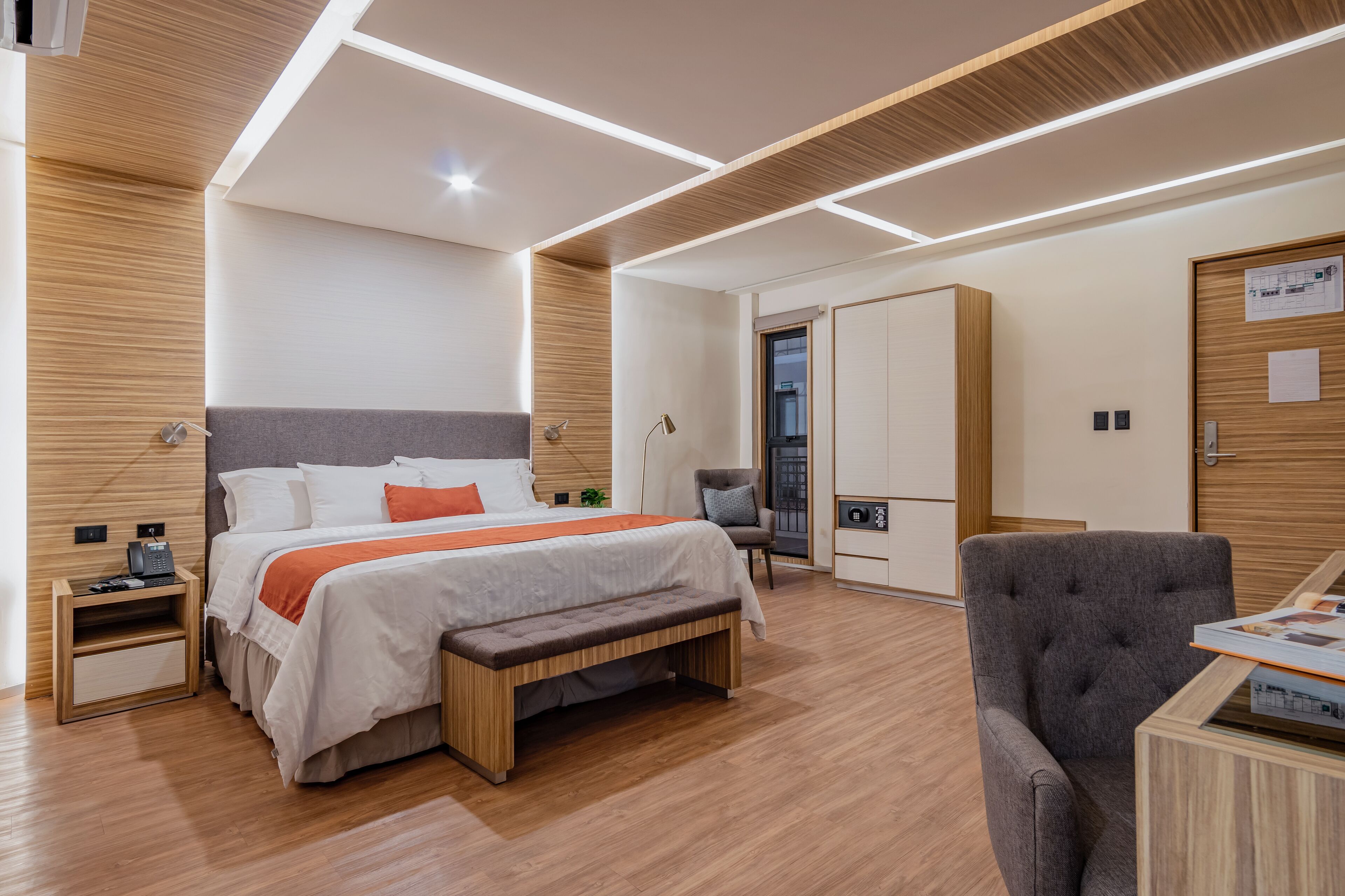 Una habitación de hotel moderna con una cama grande, un banco, un escritorio y una silla.