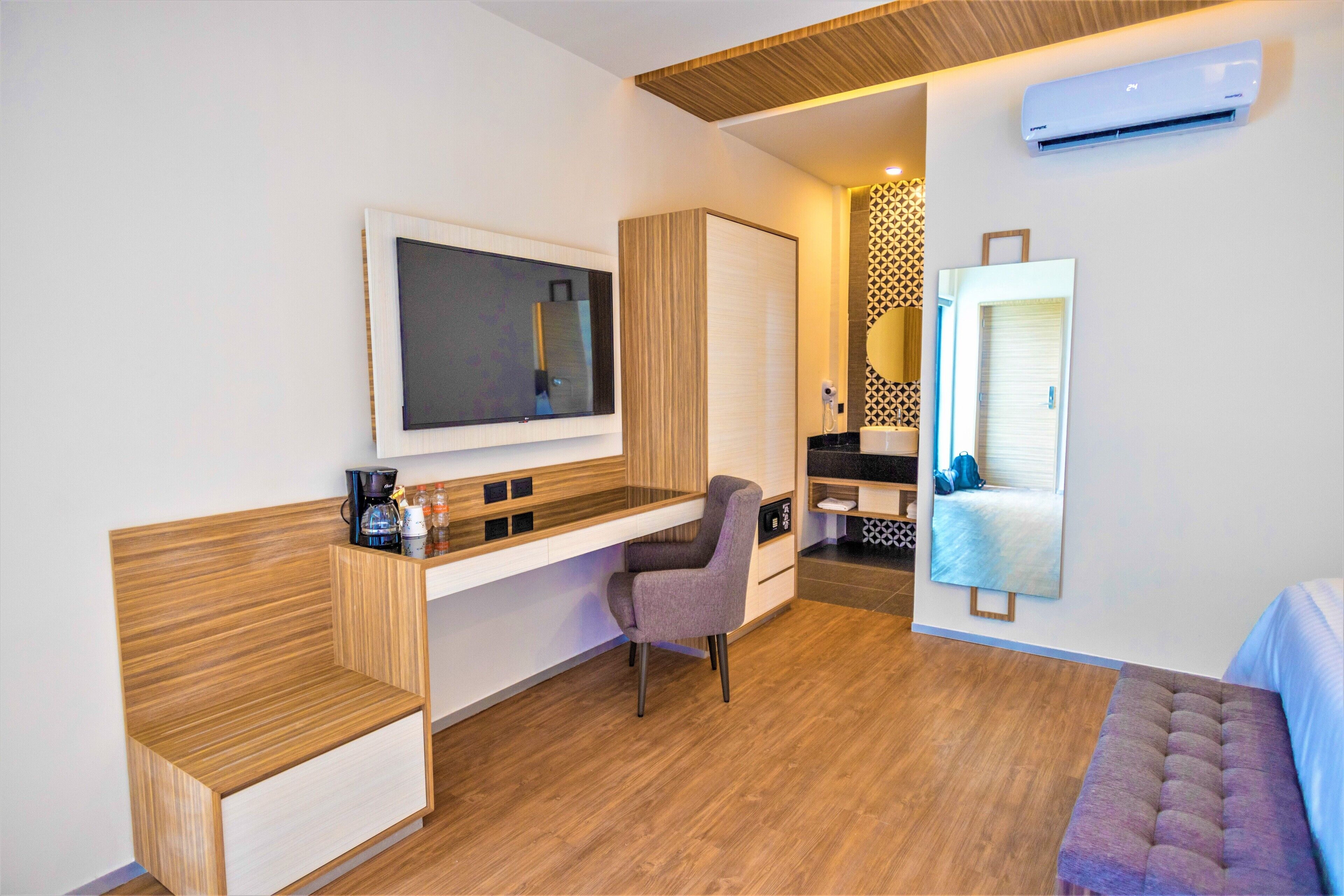A modern room with a wooden bench, a desk with a chair, a large mirror, and an air conditioning unit.