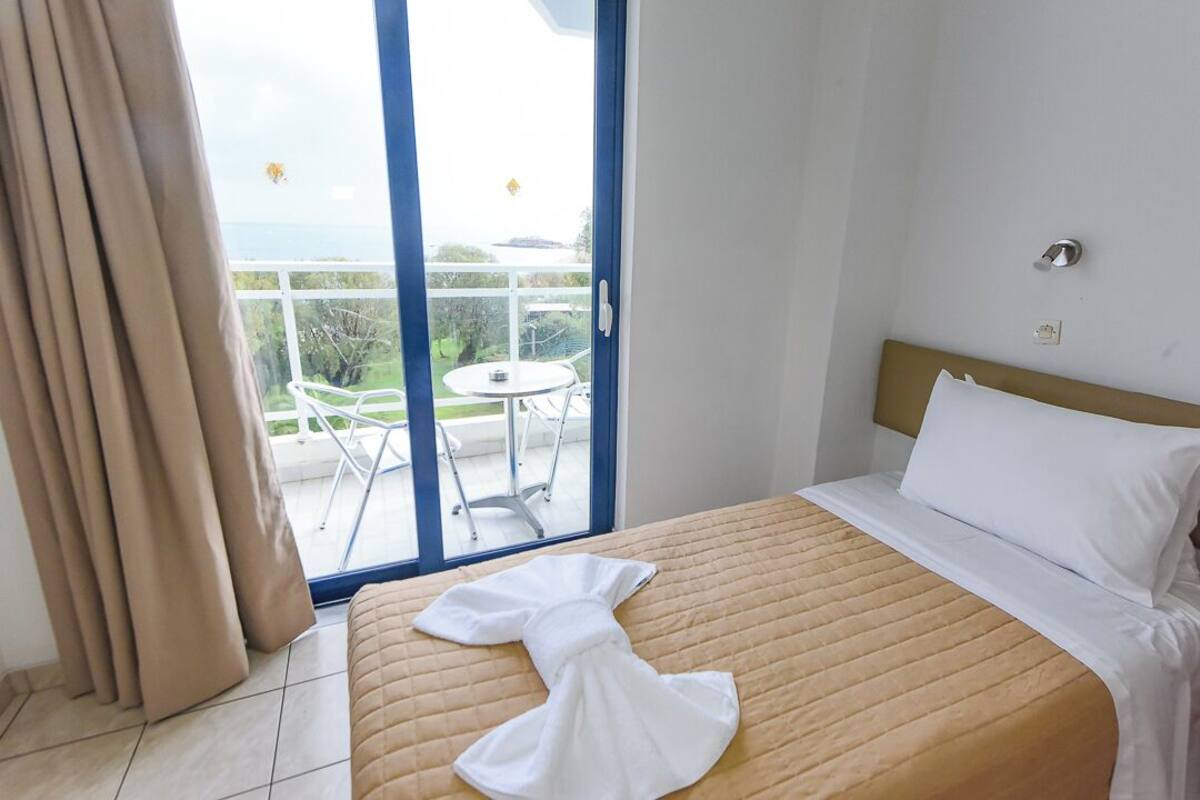 A hotel room with a bed, a view of the outdoors, and a balcony with a table and chairs.