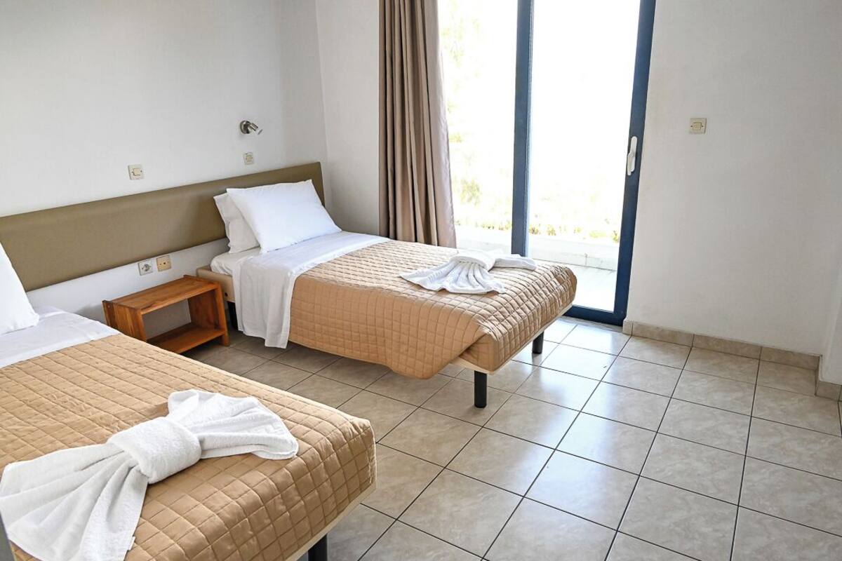 A hotel room with two beds, a wooden nightstand, a window with curtains, and a tiled floor.