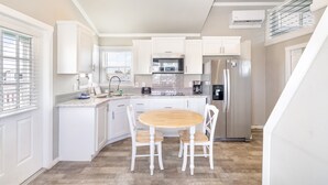 A modern kitchen with white cabinetry, stainless steel appliances, and a wooden dining table. - Tropic Island Resort (Port Aransas)