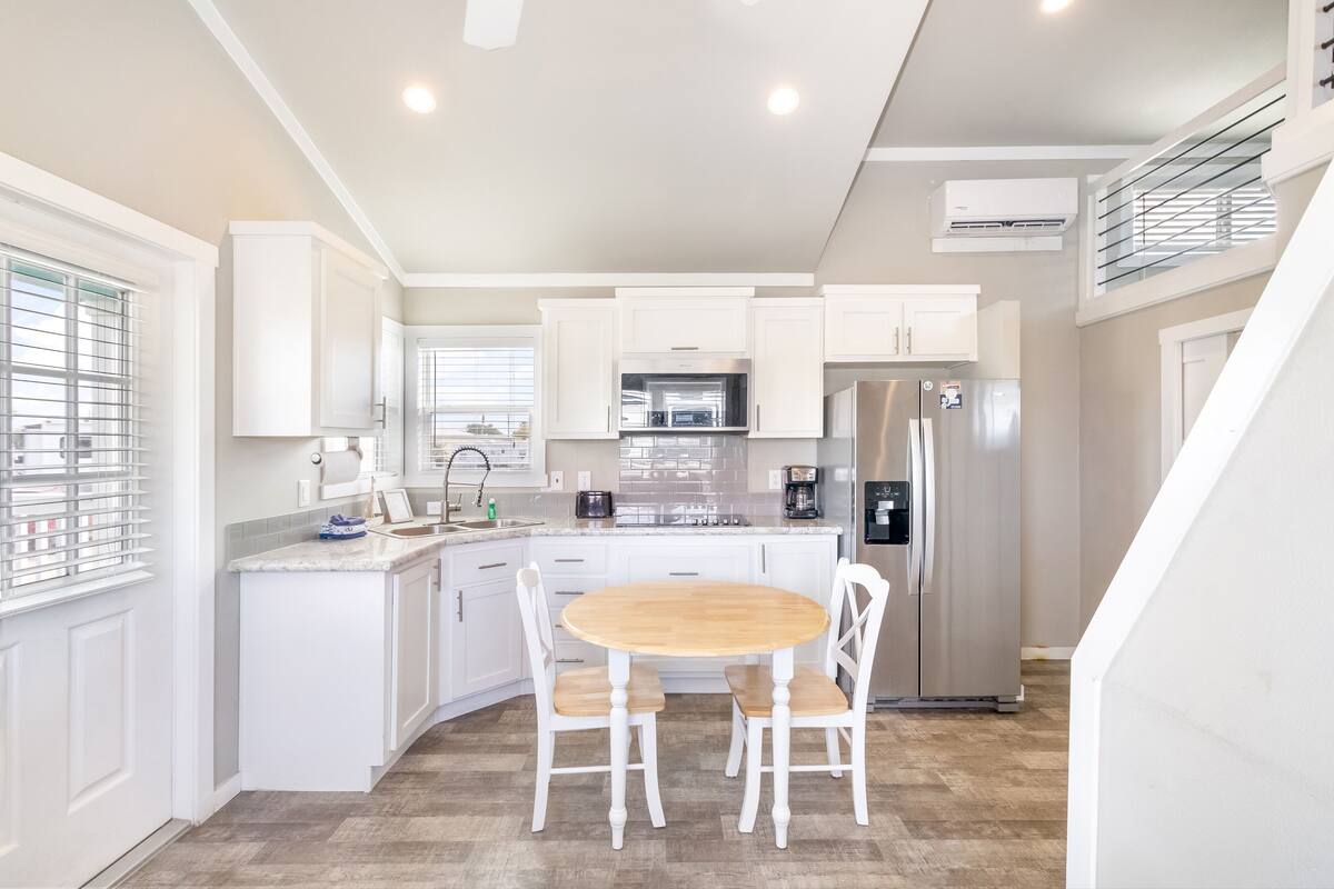 A modern kitchen with white cabinetry, stainless steel appliances, and a wooden dining table.