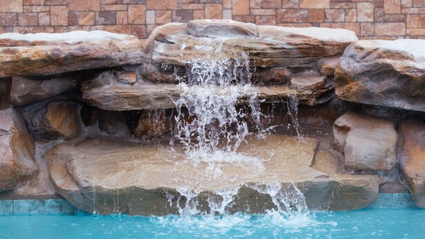 A pool with a waterfall feature surrounded by natural stone. - Tropic Island Resort (Port Aransas)