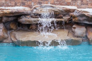 A pool with a waterfall feature surrounded by natural stone. - Tropic Island Resort (Port Aransas)