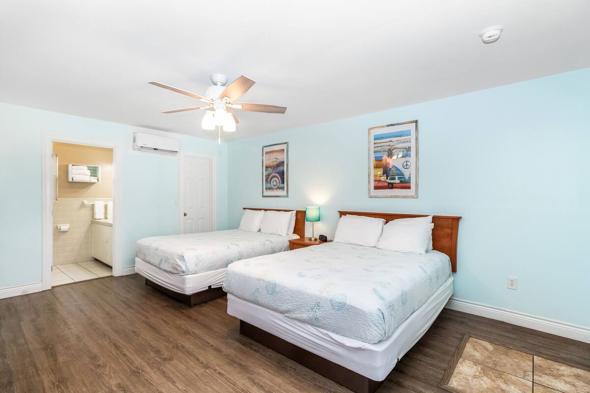 A hotel room with two beds, a ceiling fan, and artwork on the walls.