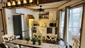Una cocina moderna con armarios blancos, electrodomésticos de acero inoxidable y una zona de comedor con mesa de madera y sillas blancas.