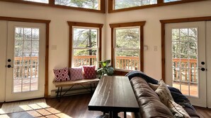 Una habitación amplia con ventanas grandes, un banco de madera, un sofá y una mesa de comedor.