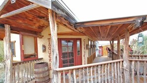Um edifício de madeira rústico com varanda, um barril de madeira e uma placa com a inscrição 'Cerveza'.