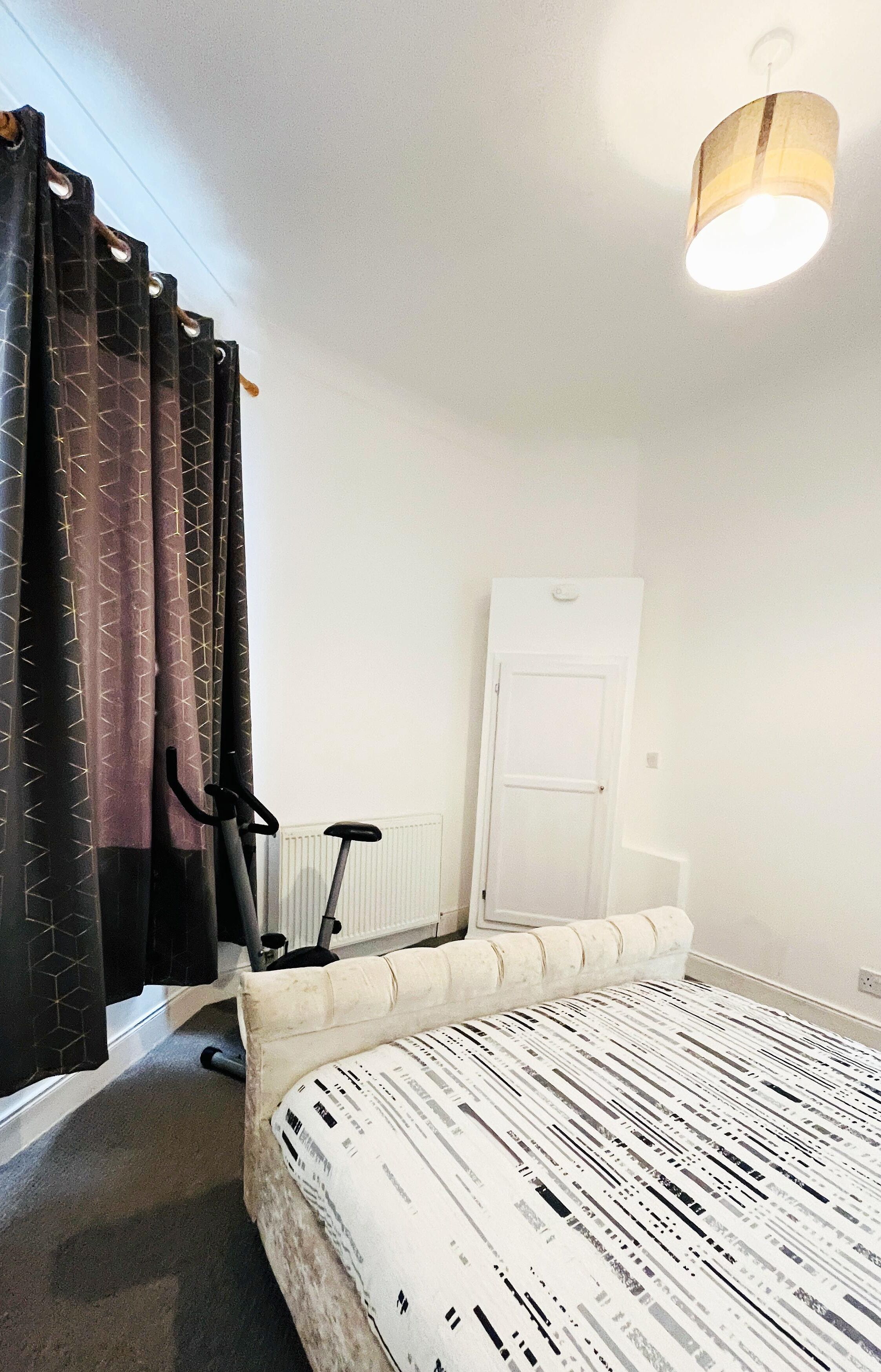 Un dormitorio con cama, ventilador, puerta y cortinas.