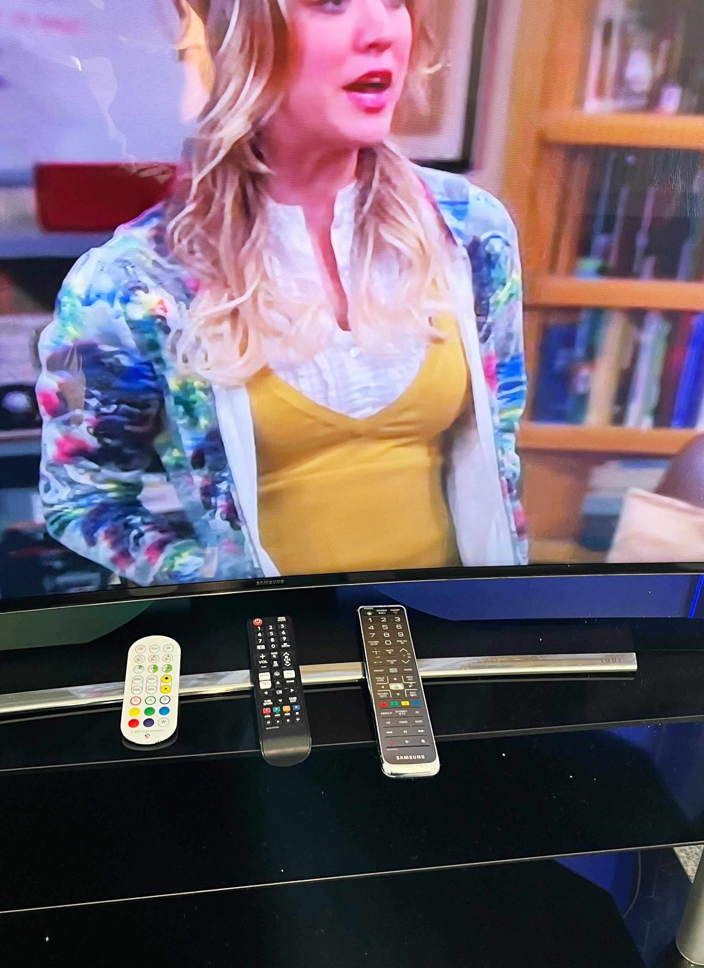 Une télévision avec deux télécommandes et une bibliothèque en arrière-plan.