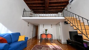 A spacious living area with a high ceiling, wooden beams, a staircase, a blue sofa, a dining table with chairs, and a television. - Cozy loft next to Spanish Steps (Roma)