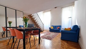 A spacious living room with a wooden floor, a dining area with orange chairs, a blue sofa, and a staircase. - Cozy loft next to Spanish Steps (Roma)