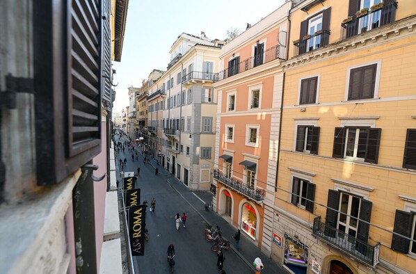 A street view with buildings, a sign for "As Roma MA", and a shop with a red awning.