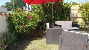 A patio area with wicker furniture, a red umbrella, and a garden with various plants.