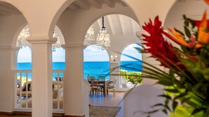 Una habitación con vista al océano, que presenta pilares blancos, candelabros y un comedor.