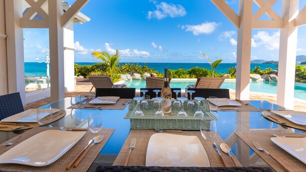 Un comedor con vistas al océano, una piscina y zona de estar exterior.