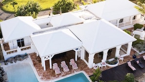 Una amplia casa con piscina, zona de estar exterior techada y abundante vegetación alrededor de la propiedad.