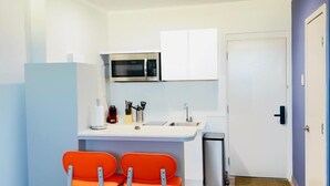 A compact kitchen with a microwave, sink, and two orange chairs. - Bushiri's Long Life Building-Studio-Sleeps 2 #2 (Oranjestad)