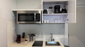 Eine kompakte Küche mit Einbau-Mikrowelle, einer Kaffeemaschine und einem Spülbecken.