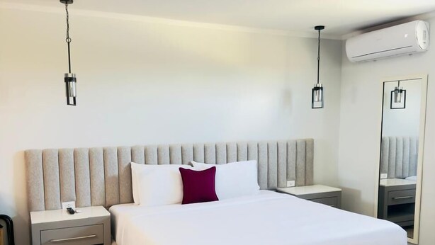 A modern hotel room with a large bed, bedside tables, an air conditioning unit, and a mirror. - Bushiri's Long Life Building-Studio-Sleeps 2 #2 (Oranjestad)