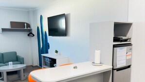 A compact kitchen with a refrigerator, a small island with a chair, a flat-screen TV mounted on the wall, and a sofa in the adjacent living area. - Bushiri's Long Life Building-Studio-Sleeps 2 #2 (Oranjestad)