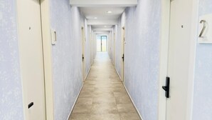 A long, narrow hallway with light blue walls and beige tiled flooring, leading to a bright room at the end. - Bushiri's Long Life Building-Studio-Sleeps 2 #2 (Oranjestad)