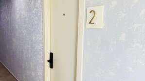 Un couloir avec une porte fermée, une plaque portant le numéro « 2 » et un mur à texture.