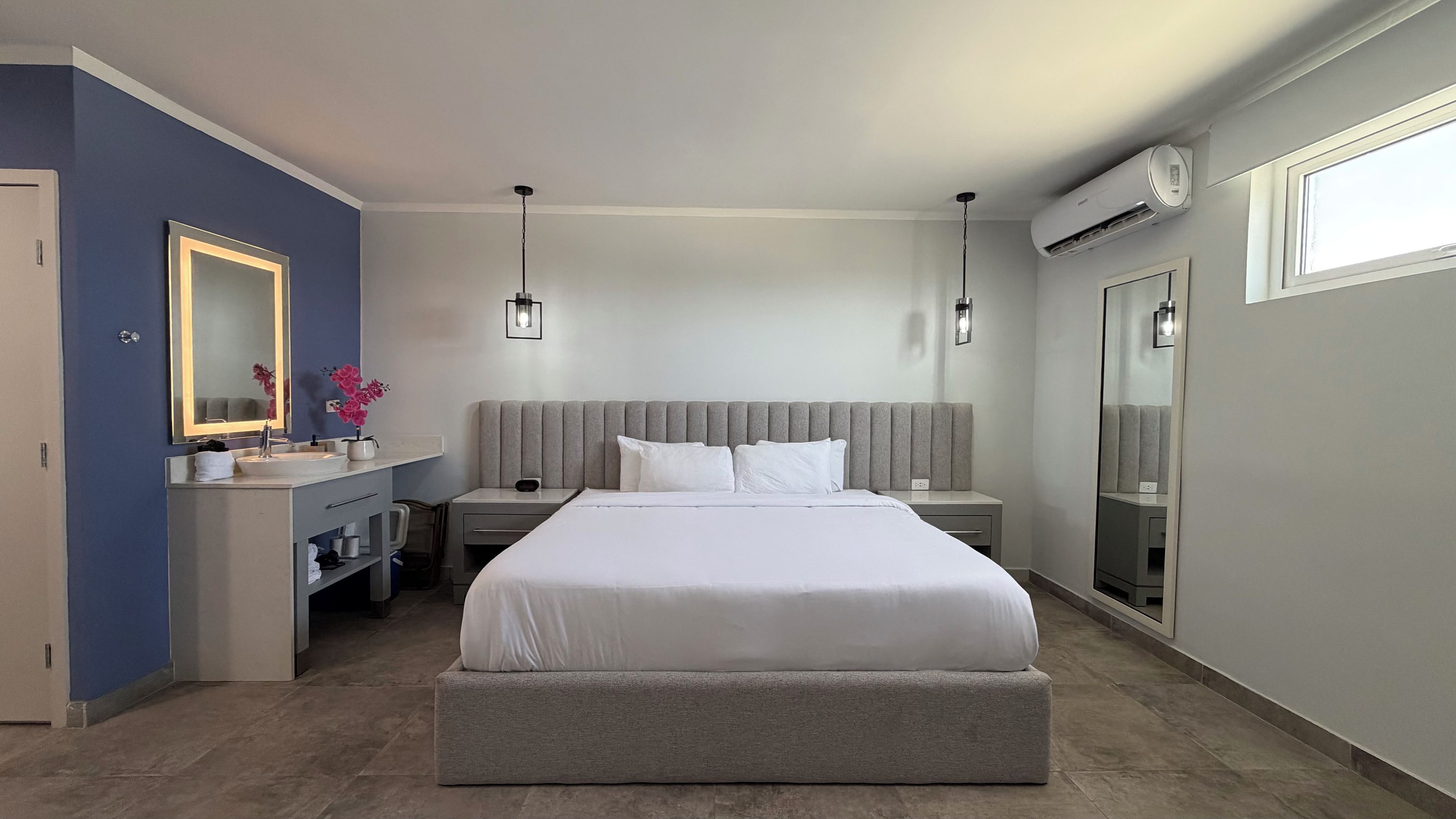 Un dormitorio moderno con una cama grande, mesitas de noche, un tocador con espejo y un equipo de aire acondicionado.