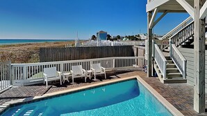 Zona de piscina con vistas a la playa, sillas de deck blancas y una valla de madera.
