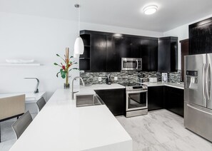Uma cozinha moderna com armários pretos, eletrodomésticos de aço inoxidável, bancada branca e painel de azulejos.