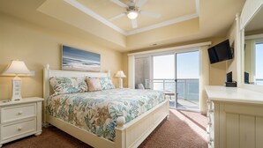A bedroom with a bed, a ceiling fan, a TV, and a balcony with a view.