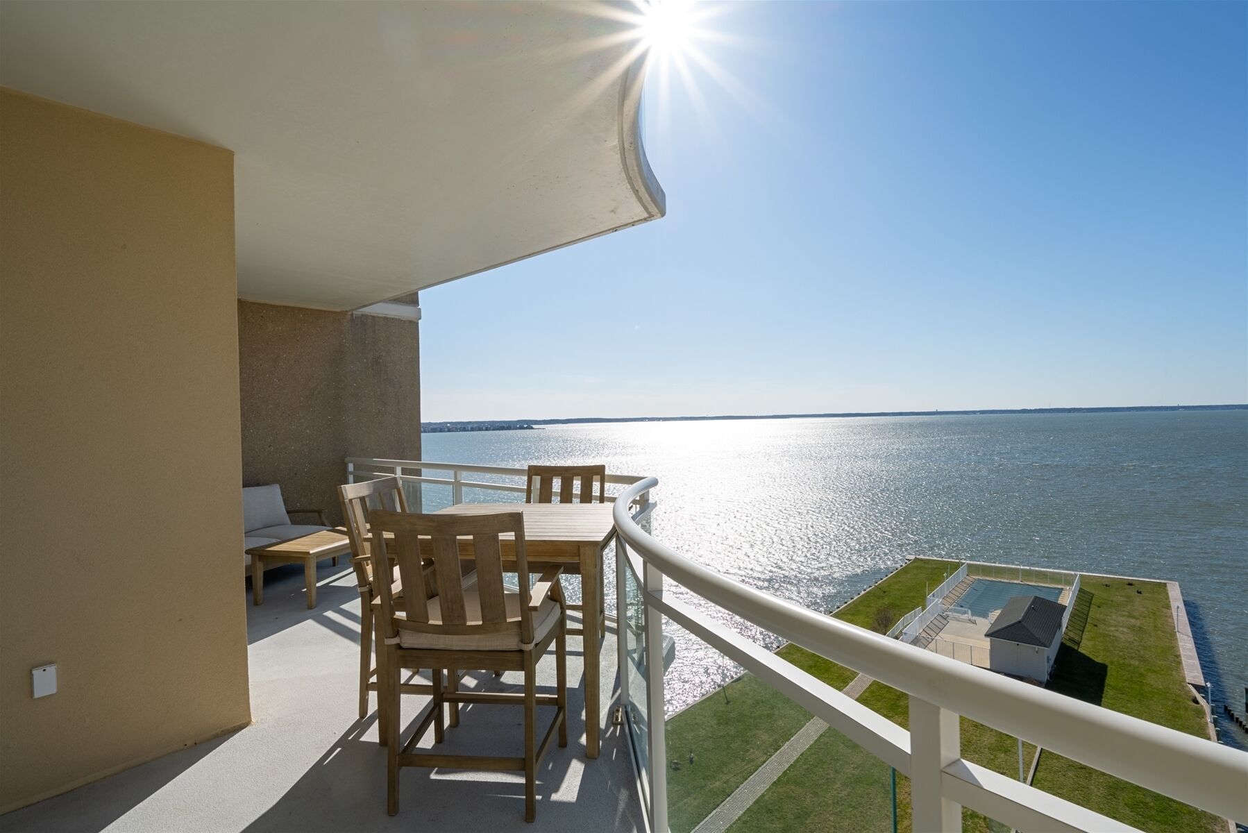 A balcony with a wooden table and chairs, overlooking a body of water.