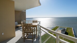 A balcony with a wooden table and chairs, overlooking a body of water.